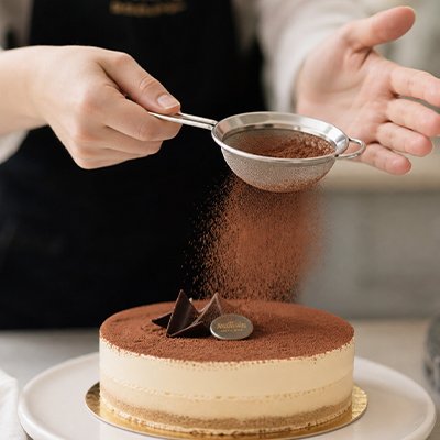 Saupoudrage poudre chocolat avec Tamis sur gâteau